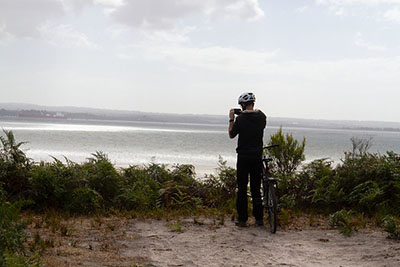 A man stands with a bike, taking a photo of a view on French Island. Discover 10 day trips from Melbourne by train.